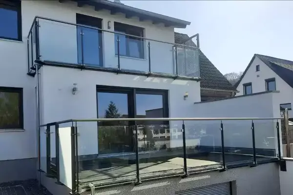 Modernes Einfamilienhaus mit Glasbalkon und großem Terrassenbereich im Sonnenlicht.